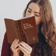 Woman reading a brown book titled 'Living Our Faith Day by Day' against a white background