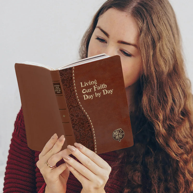 Woman reading a brown book titled 'Living Our Faith Day by Day' against a white background