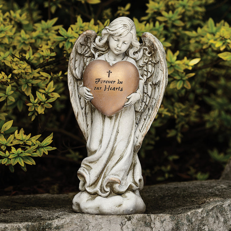 Statue of a memorial angel holding a gold heart with text, outdoors.