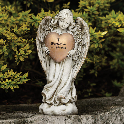 Statue of a memorial angel holding a gold heart with text, outdoors.