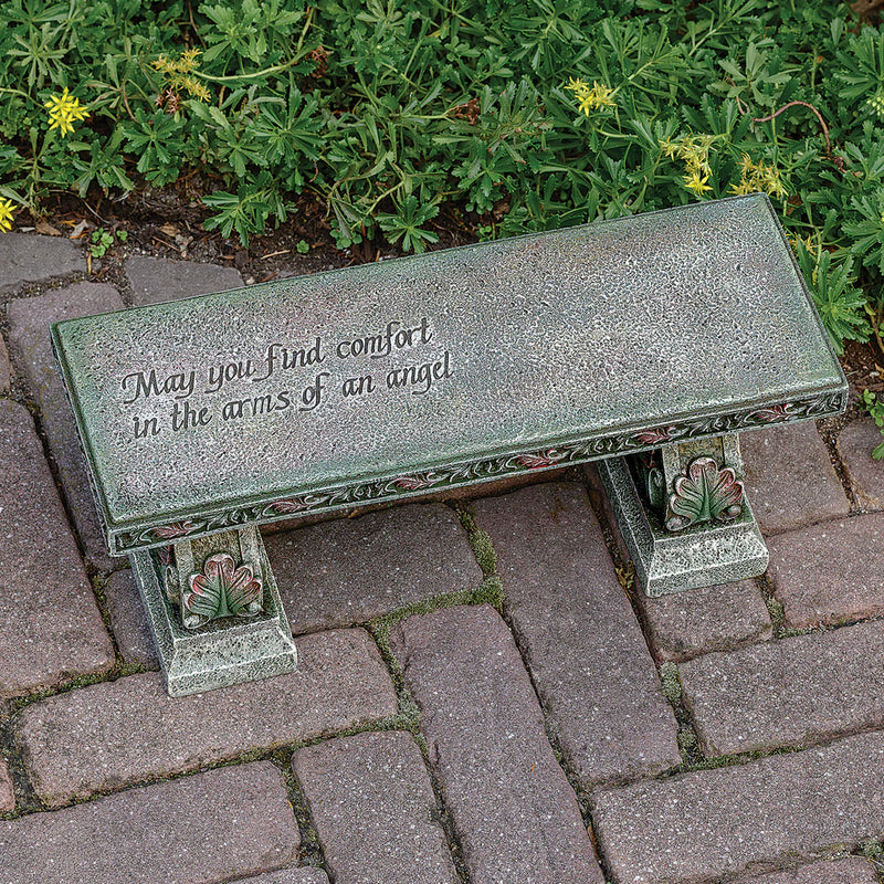 Decorative bench with engraved text on a paved area with greenery