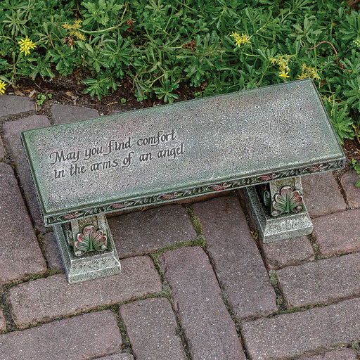 Decorative bench with engraved text on a paved area with greenery