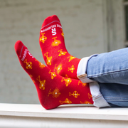 Person wearing vibrant red and gold socks featuring images of different monstrances with the Blessed Sacrament