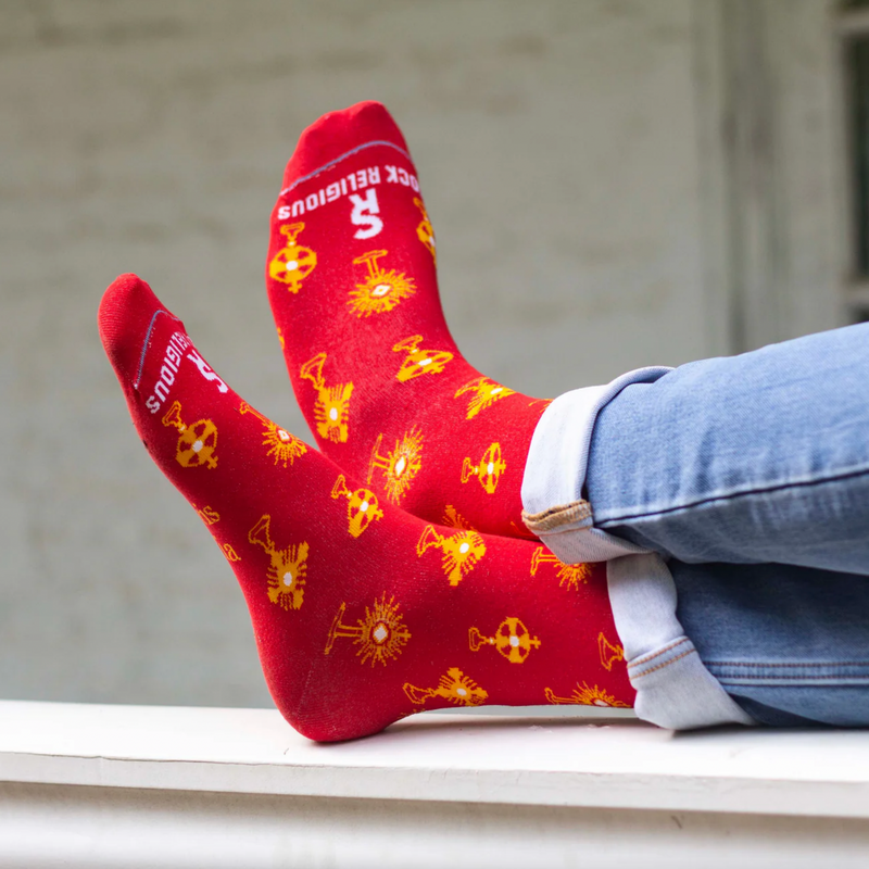 Person wearing vibrant red and gold socks featuring images of different monstrances with the Blessed Sacrament