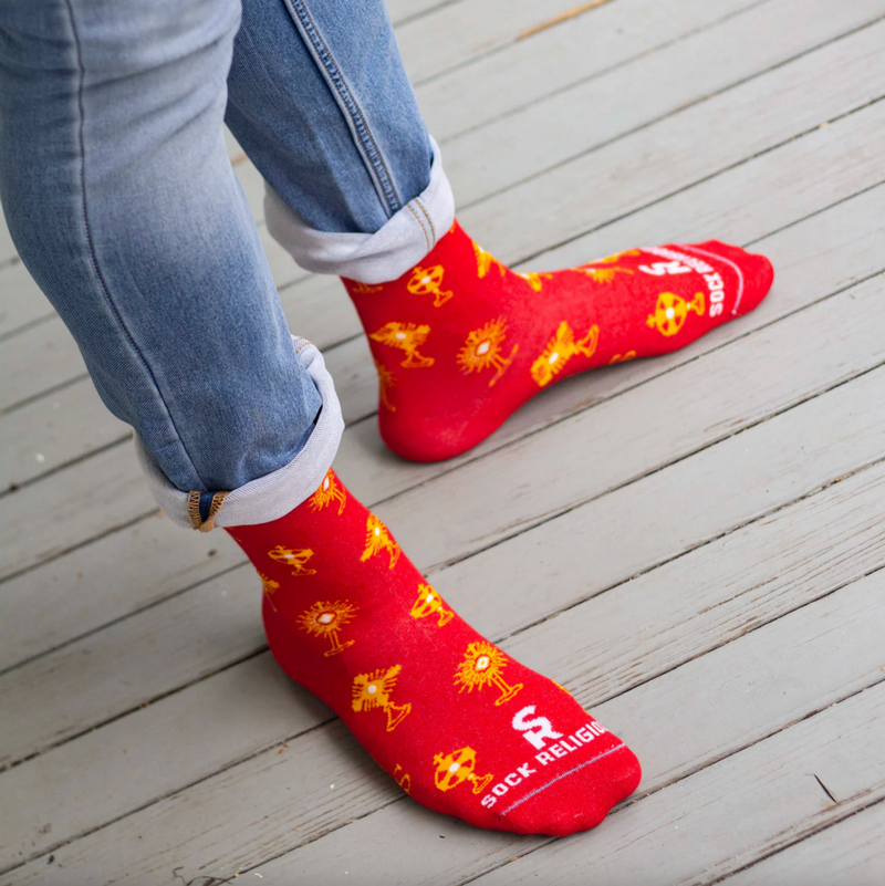 Person wearing vibrant red and gold socks featuring images of different monstrances with the Blessed Sacrament