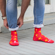 Person wearing vibrant red and gold socks featuring images of different monstrances with the Blessed Sacrament