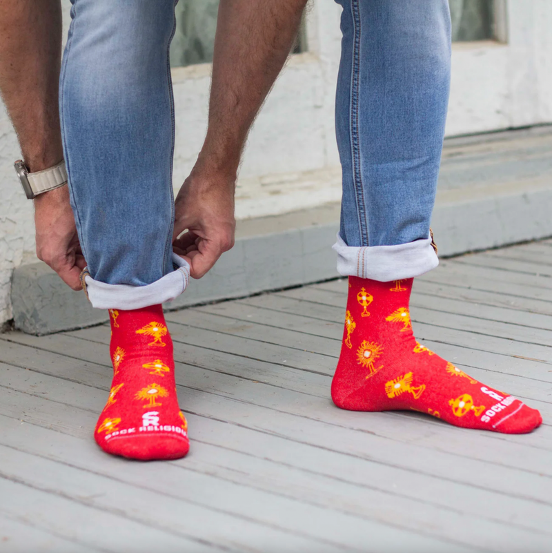 Person wearing vibrant red and gold socks featuring images of different monstrances with the Blessed Sacrament