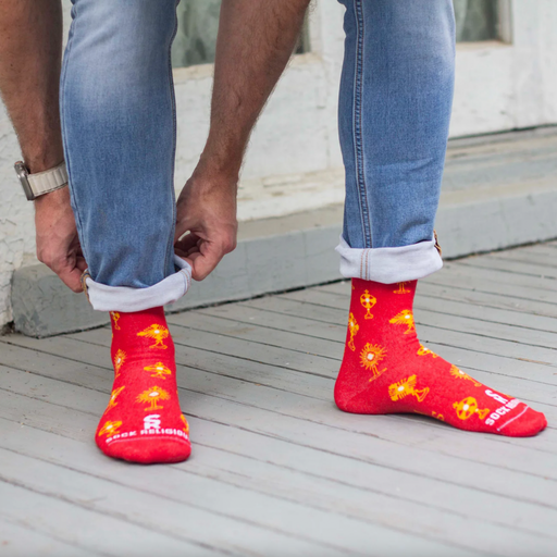 Person wearing vibrant red and gold socks featuring images of different monstrances with the Blessed Sacrament