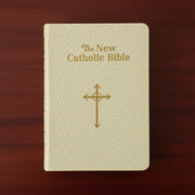 Beige Bible with 'The New Catholic Bible' text and cross symbol on a wooden surface