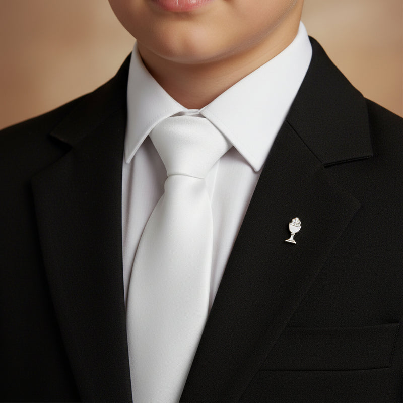 First Communicant boy wearing a black suit with a white shirt and tie, featuring a small decorative pin on the lapel.