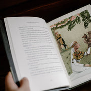 Open book with illustrated page and text, held by a hand.