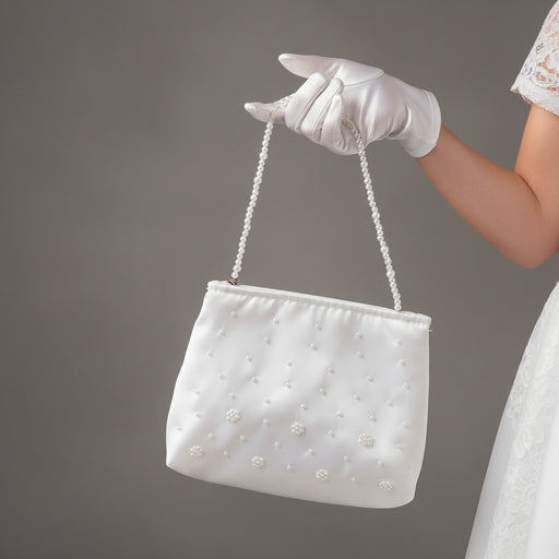 White First Communion handbag with pearl embellishments held by a gloved hand against a gray background