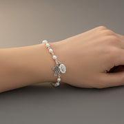 Pearl bracelet with charms on a wrist against a neutral background