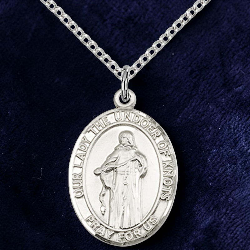 Silver religious pendant on a chain against a dark blue background