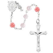A pink crystal First Communion rosary in a white box, with rose Our Father beads and a pewter Miraculous Medal centerpiece.