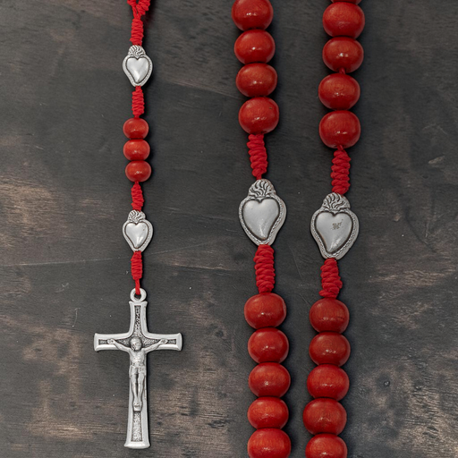 Red beaded rosary with silver heart-shaped beads and crucifix on a dark wooden surface