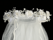 Close-up view of a white communion veil with corded flowers, pearls, and rhinestones, featuring a satin bow at the back.