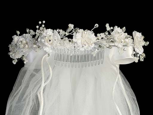 Close-up view of a white communion veil with corded flowers, pearls, and rhinestones, featuring a satin bow at the back.