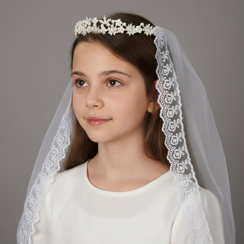 Young girl wearing a white lace First Communion veil and tiara against a gray background