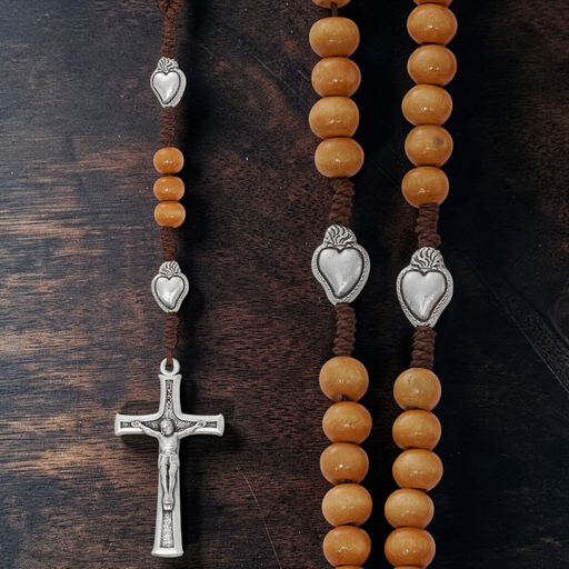 Two rosaries with tan beads and silver heart charms on a dark wooden surface.