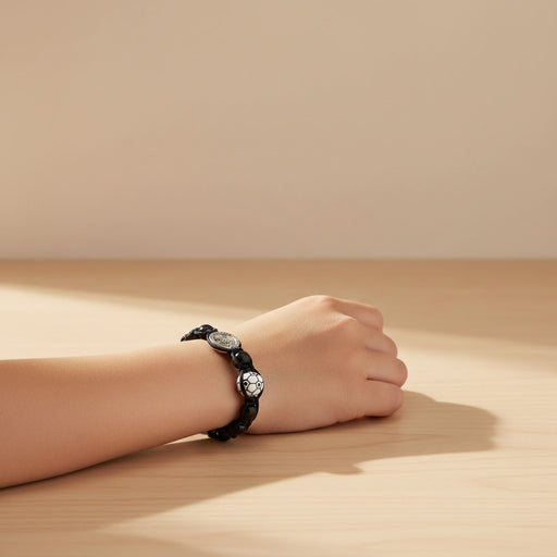Hand wearing a black bracelet on a wooden surface with a beige background