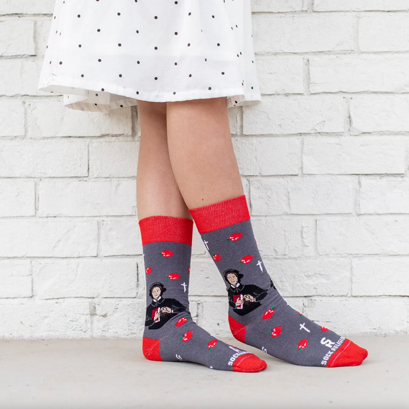 Person wearing red and gray sock featuring pictures of apples and St. Elizabeth Ann Seton