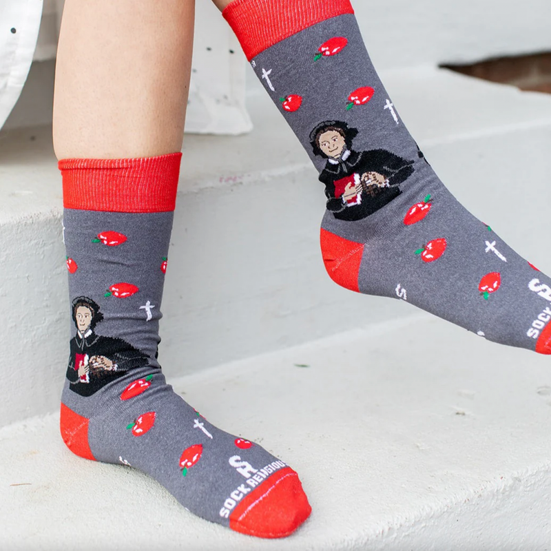 Person wearing red and gray sock featuring pictures of apples and St. Elizabeth Ann Seton