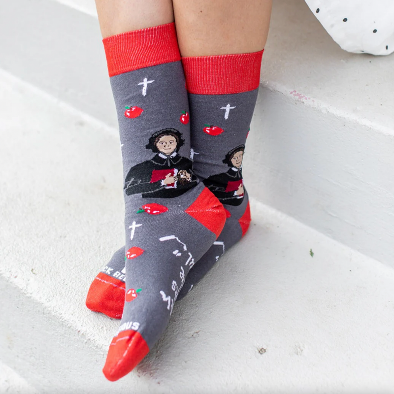 Person wearing red and gray sock featuring pictures of apples and St. Elizabeth Ann Seton