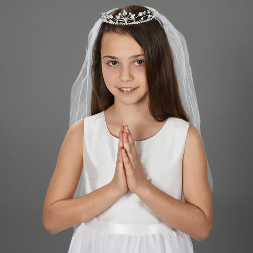 A young girl with hands folded in prayer wears a white communion veil with a jeweled tiara
