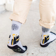 Gray socks with St. Benedict design worn by a person on a light gray pavement background