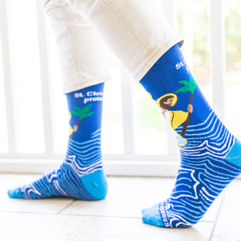 Person wearing blue socks with images of St. Christopher carrying the Infant Jesus through water