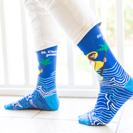 Person wearing blue socks with images of St. Christopher carrying the Infant Jesus through water