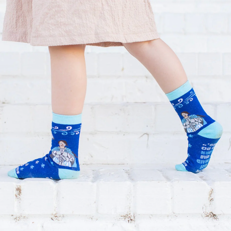 Child wearing blue crew socks featuring a fleur-de-lis pattern and an image of St. Joan of Arc holding a sword