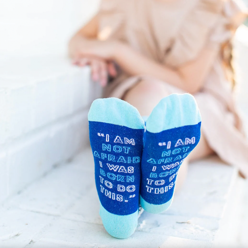 Child wearing blue crew socks featuring a fleur-de-lis pattern and an image of St. Joan of Arc holding a sword