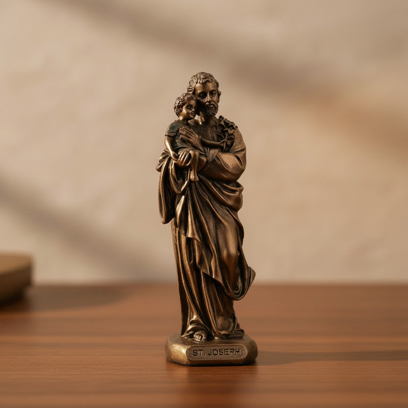 Bronze statue of St. Joseph holding Baby Jesus on a wooden surface with a blurred background