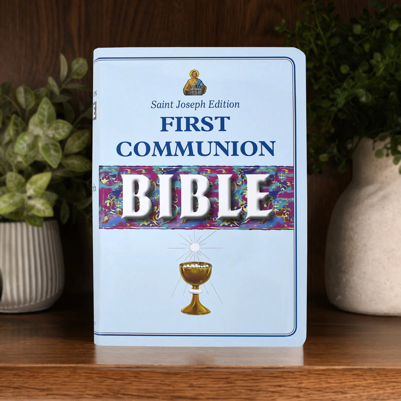 Saint Joseph Edition First Communion Bible on a wooden surface with plants in the background