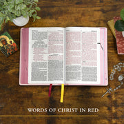 Open book with pink cover on a wooden surface, surrounded by decorative items.