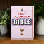 First Communion Bible with colorful design on a wooden surface with plants in the background