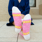 Person wearing pink and gold socks featuring an image of St. Philomena holding a palm branch