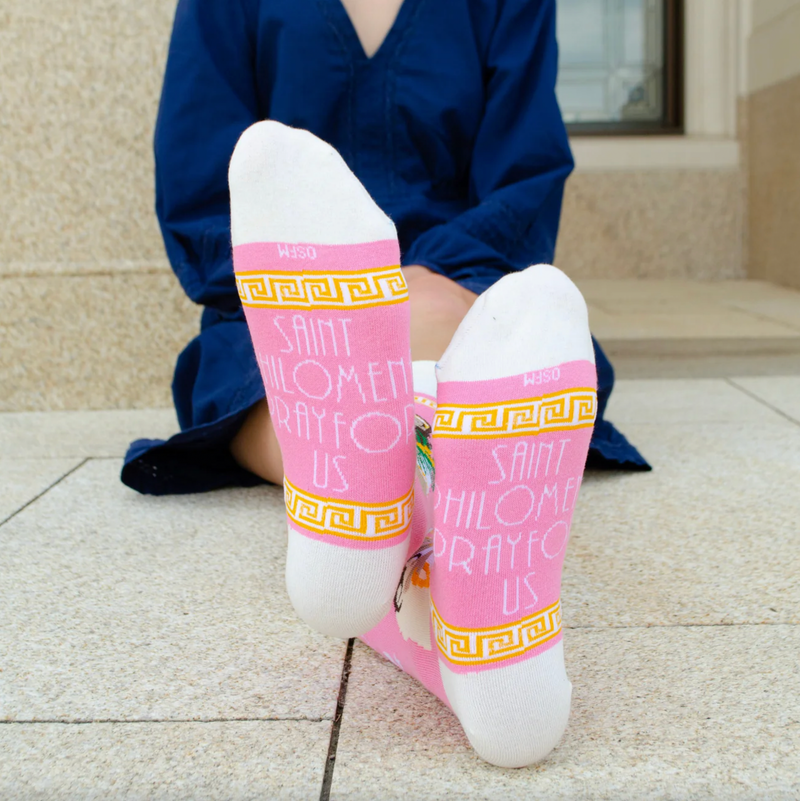 Person wearing pink and gold socks featuring an image of St. Philomena holding a palm branch