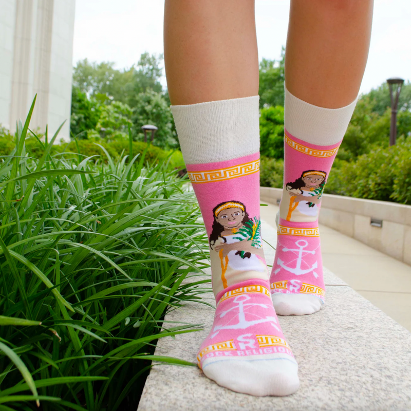 Person wearing pink and gold socks featuring an image of St. Philomena holding a palm branch