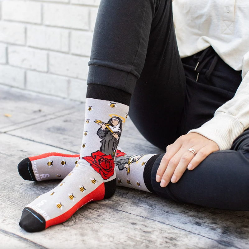 Person wearing gray socks with vibrant red roses and an image of St. Rita holding a cross.