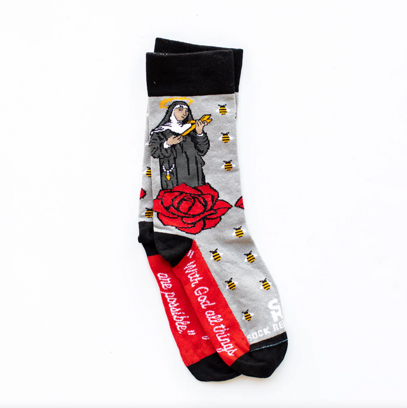 A pair of adult-sized socks featuring an illustration of St. Rita with a red rose and bees on her head, with the text 'With God, all things are possible.
