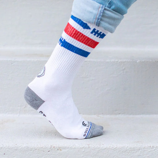 White St. Sebastian socks with blue and red stripes worn with light blue jeans on a light gray background