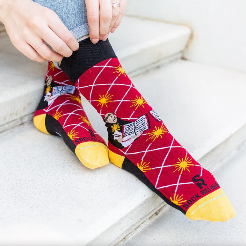 Person wearing bright red socks with an image of St. Thomas Aquinas holding an open book