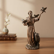 Bronze statue of a religious figure holding doves and a lamb on a wooden surface with a neutral background.