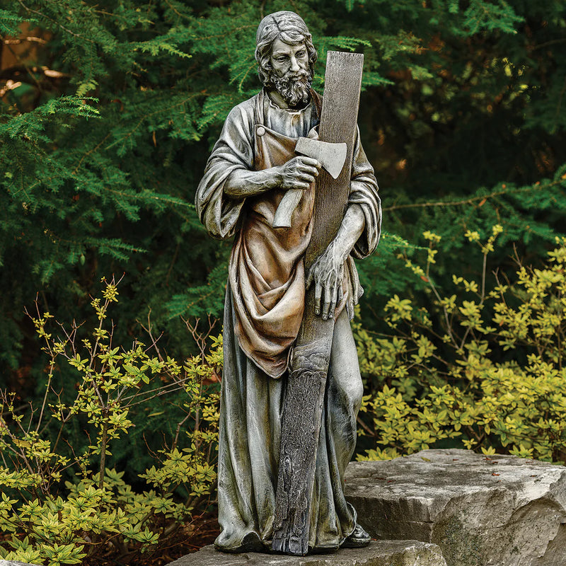 Statue of a bearded man holding a cross in a garden setting
