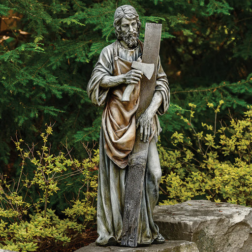 Statue of a bearded man holding a cross in a garden setting