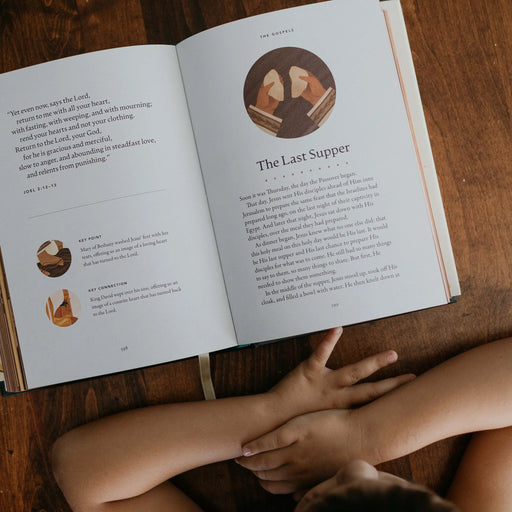 Open book on a wooden surface with illustrations and text, accompanied by a person's hands.