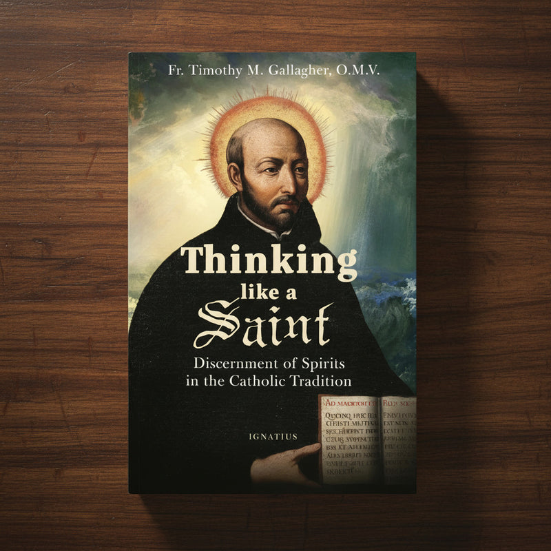 Dark-colored paperback book entitled 'Thinking Like a Saint' with an image of St. Ignatius of Loyola, on a dark wood background.